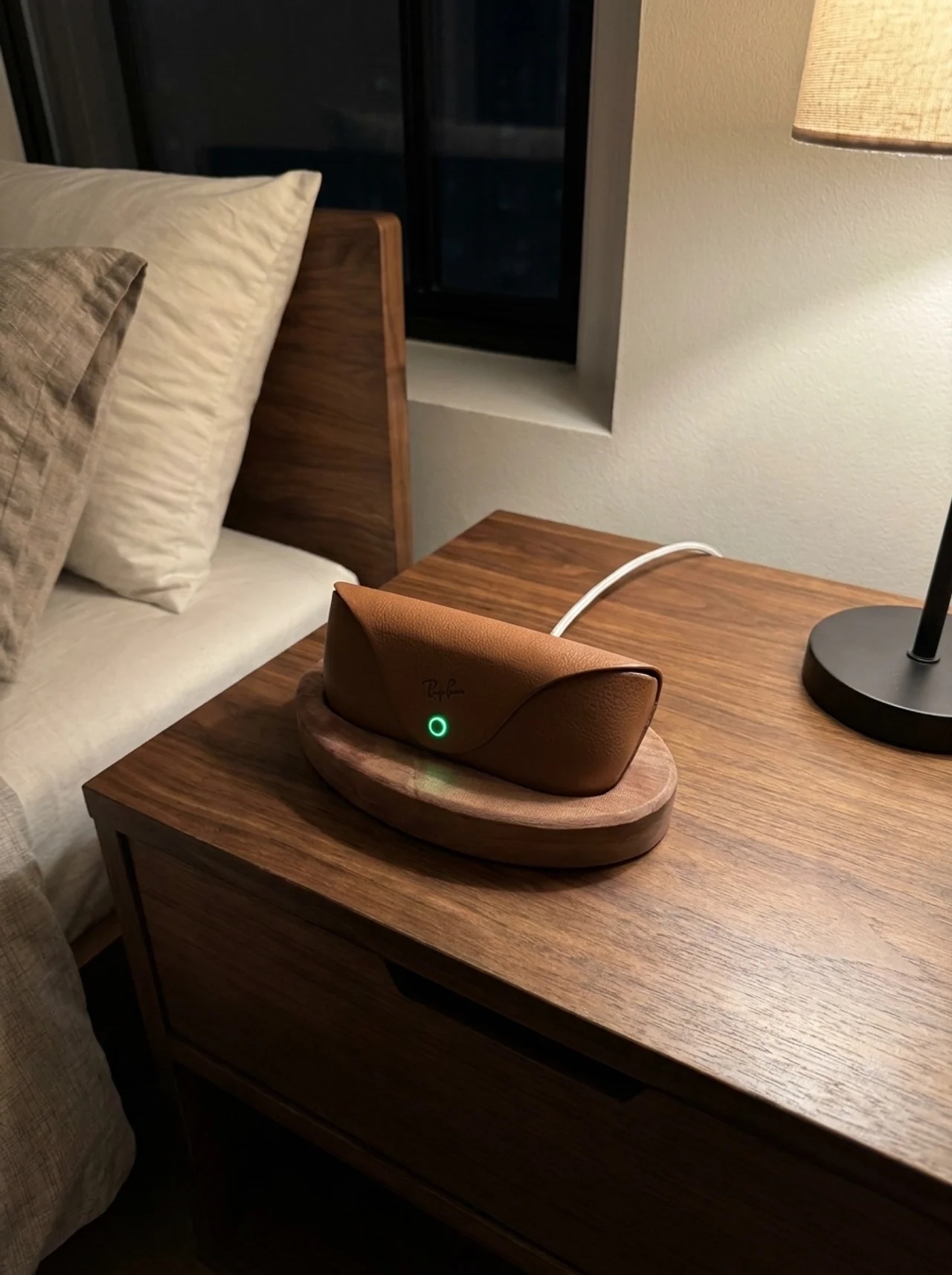 Ray-Ban Meta case docked on the walnut stand at night, charge light glowing green